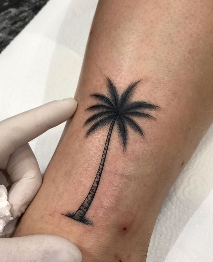 a small palm tree tattoo on the left arm and wrist is shown in black ink