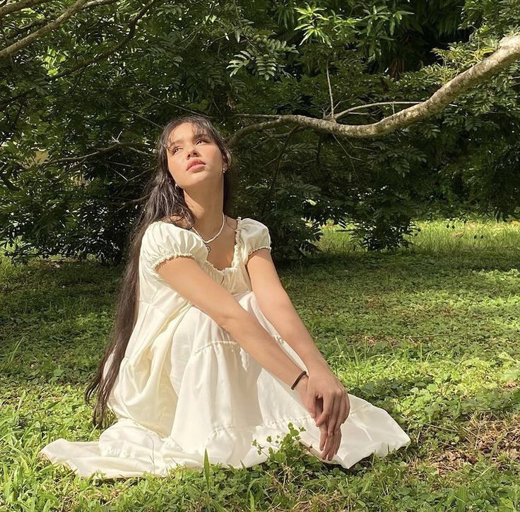 a woman sitting in the grass with her eyes closed and hands on her knees looking up