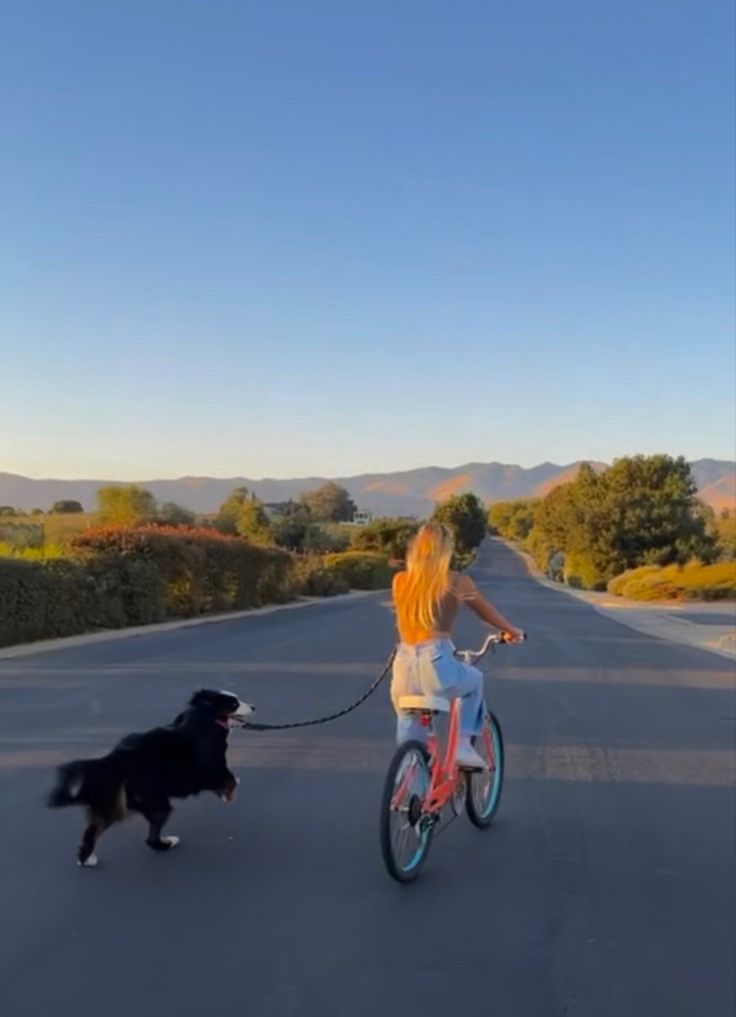 a woman riding a bike with a dog on a leash