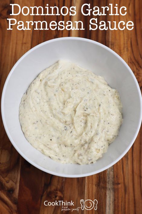 a white bowl filled with garlic sauce on top of a wooden table next to a spoon