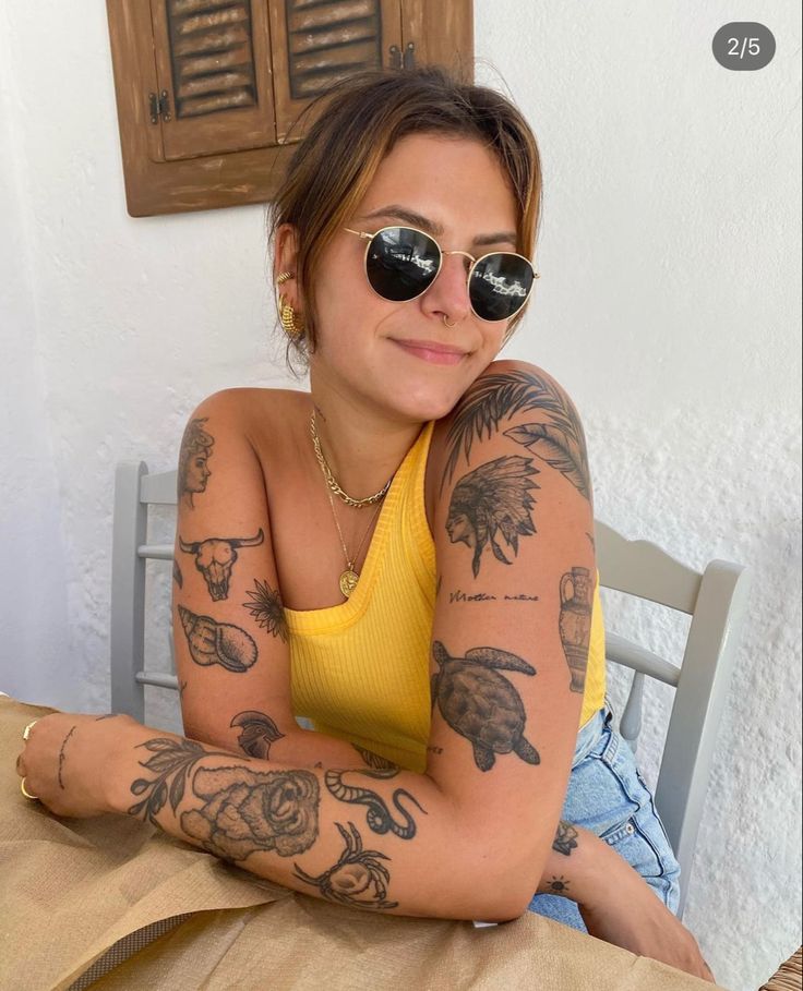 a woman sitting at a table with tattoos on her arm