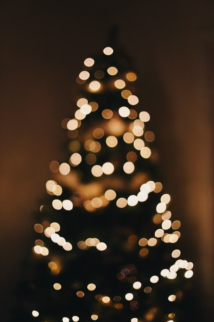 a lit up christmas tree with blurry lights on the top and bottom branches, in front of a dark background