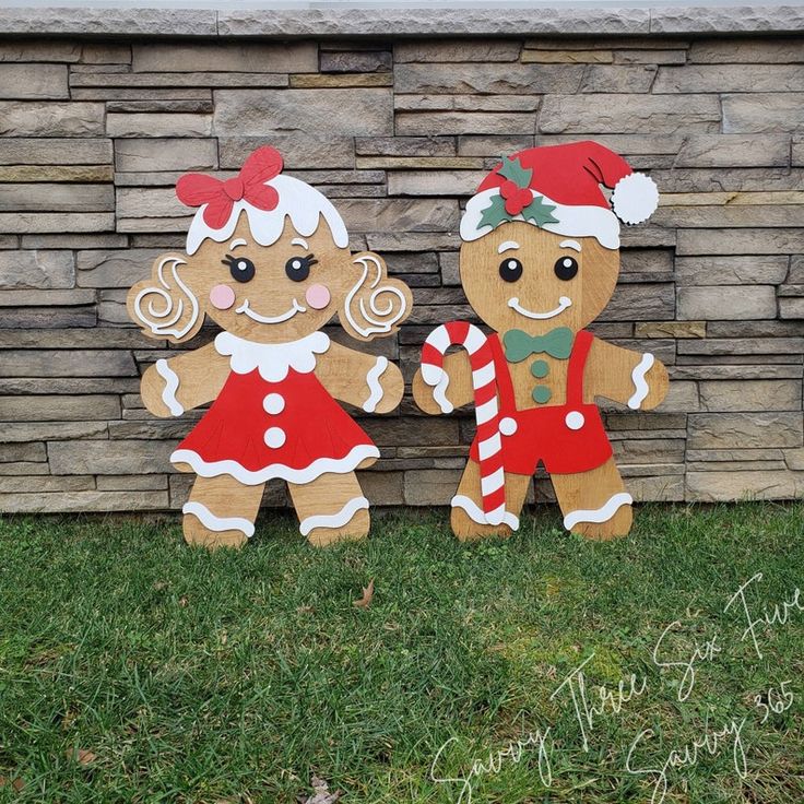 two gingerbread man and woman standing in front of a brick wall with christmas decorations