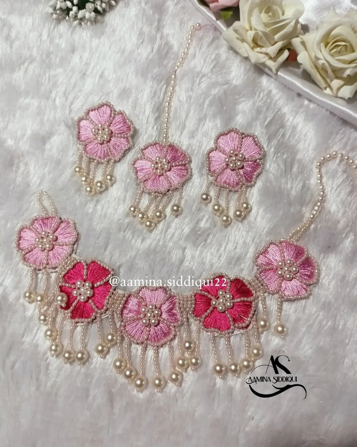 pink flower necklace and earrings set with pearls on white furnishing next to flowers