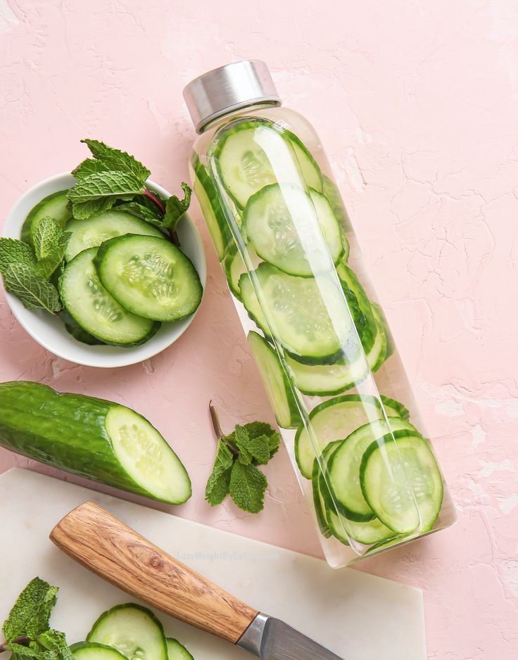 cucumber slices and mint leaves in a jar next to a knife