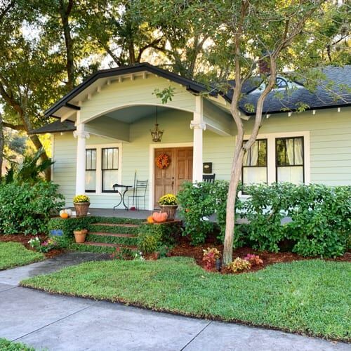 a house that is sitting in the grass with flowers and plants growing around it's front yard