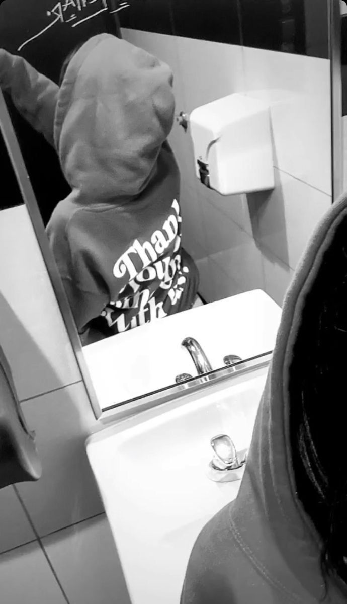 a person wearing a hoodie taking a selfie in a bathroom mirror with graffiti on the wall