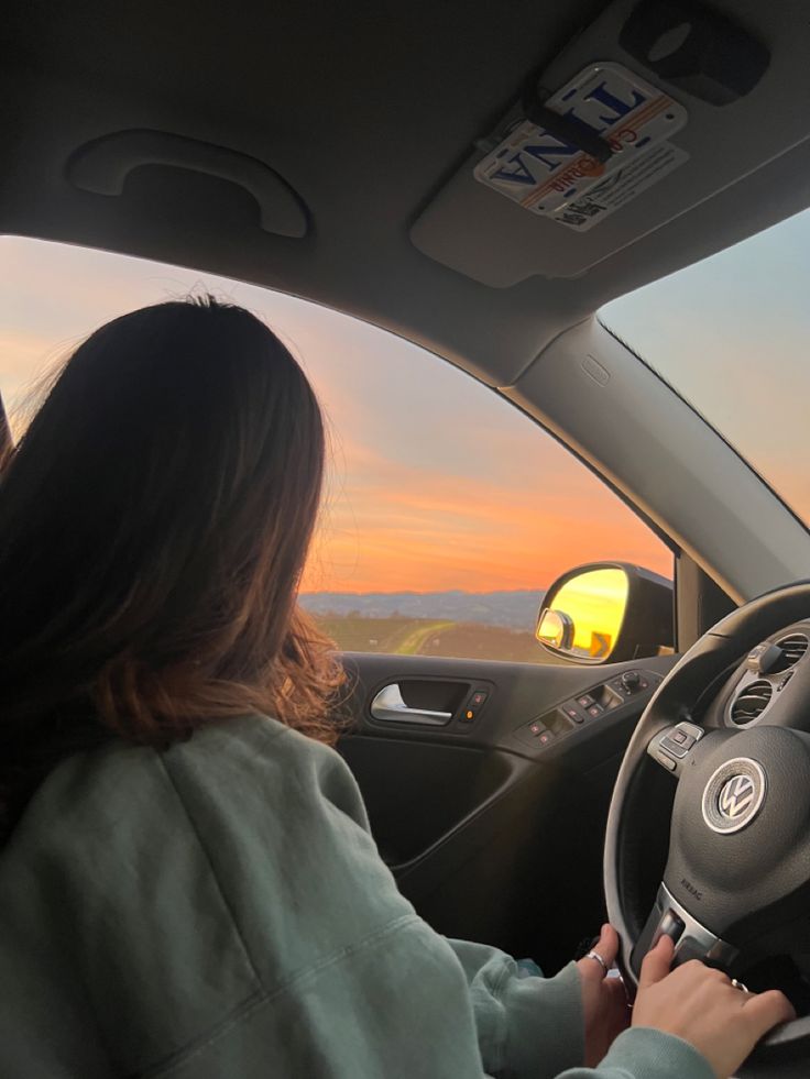 the woman is driving her car at sunset