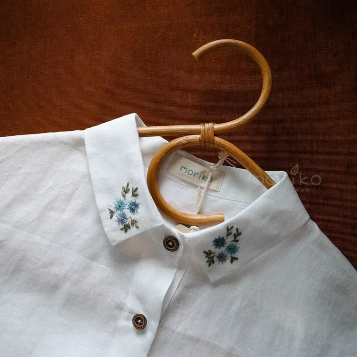 a white shirt with blue flowers is hanging on a wooden hanger and has an umbrella attached to it