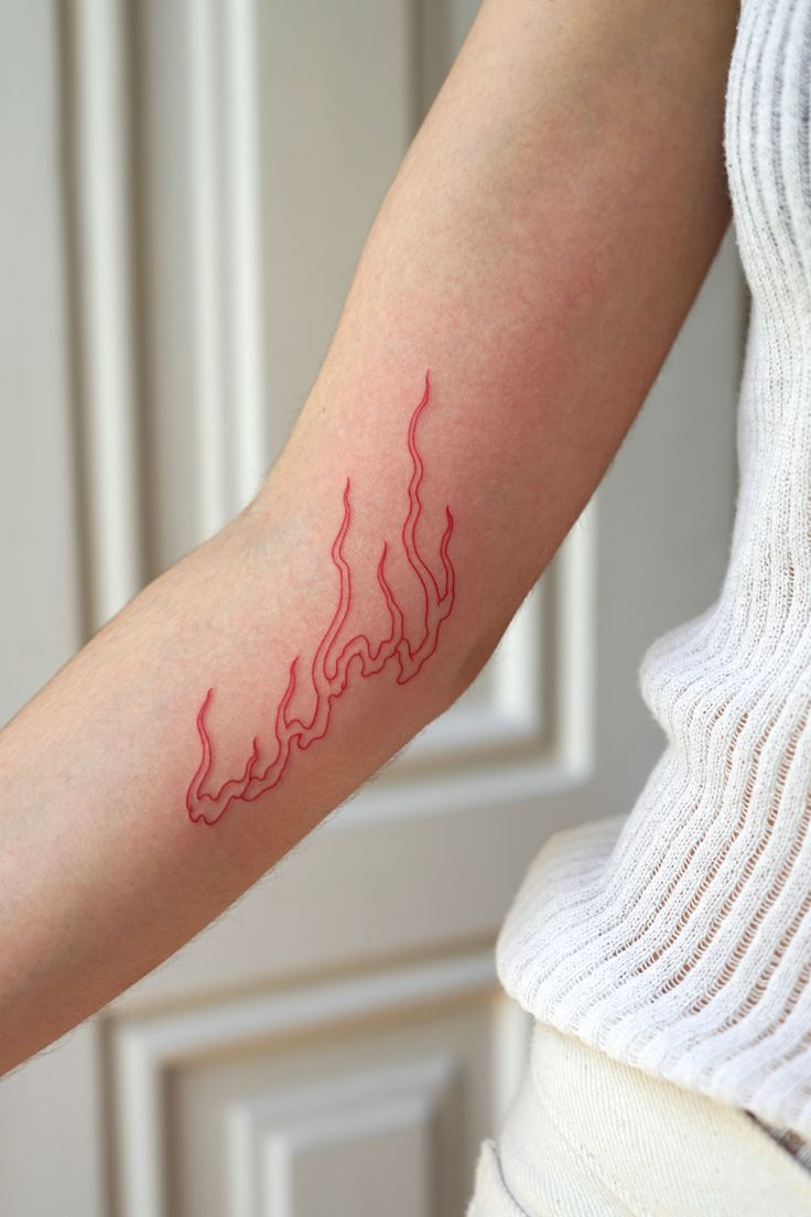 a woman's arm with a red fire tattoo on the left side of her arm