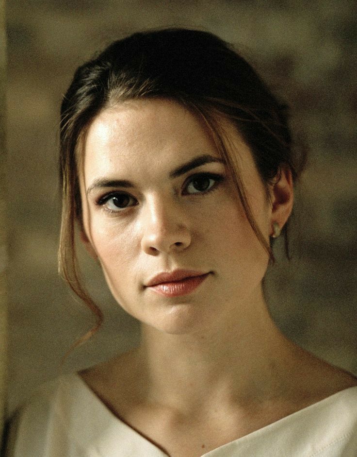 a woman in a white dress is looking at the camera and has her hair pulled back