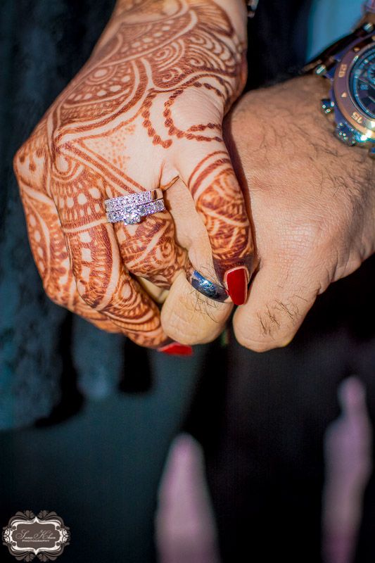 two people holding hands with henna tattoos on their arms and wrist, both wearing wedding rings