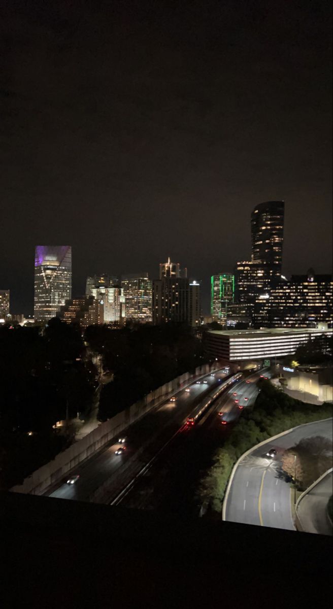 the city skyline is lit up at night, with cars driving on the road below