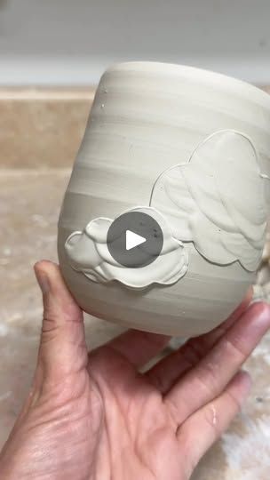 a hand holding a white vase with clouds painted on the side and a video playing below it