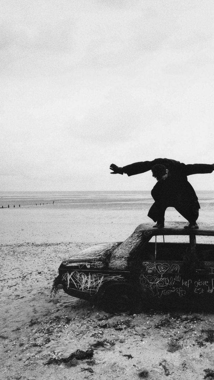 a man standing on top of an old car in the middle of nowhere with his arms outstretched