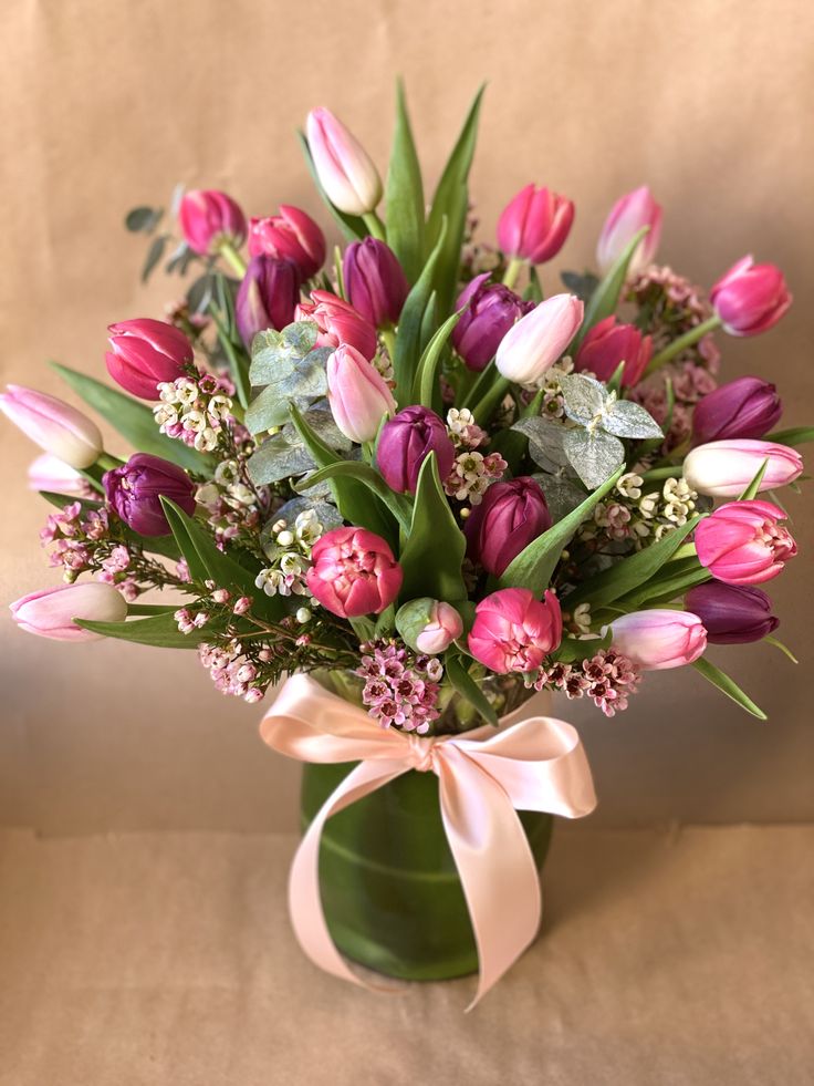 a bouquet of tulips and other flowers in a green vase with a pink ribbon