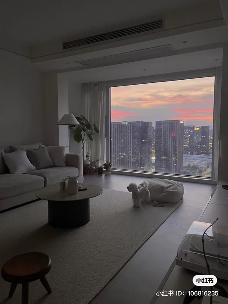 a living room filled with furniture and a large window overlooking the cityscape at sunset