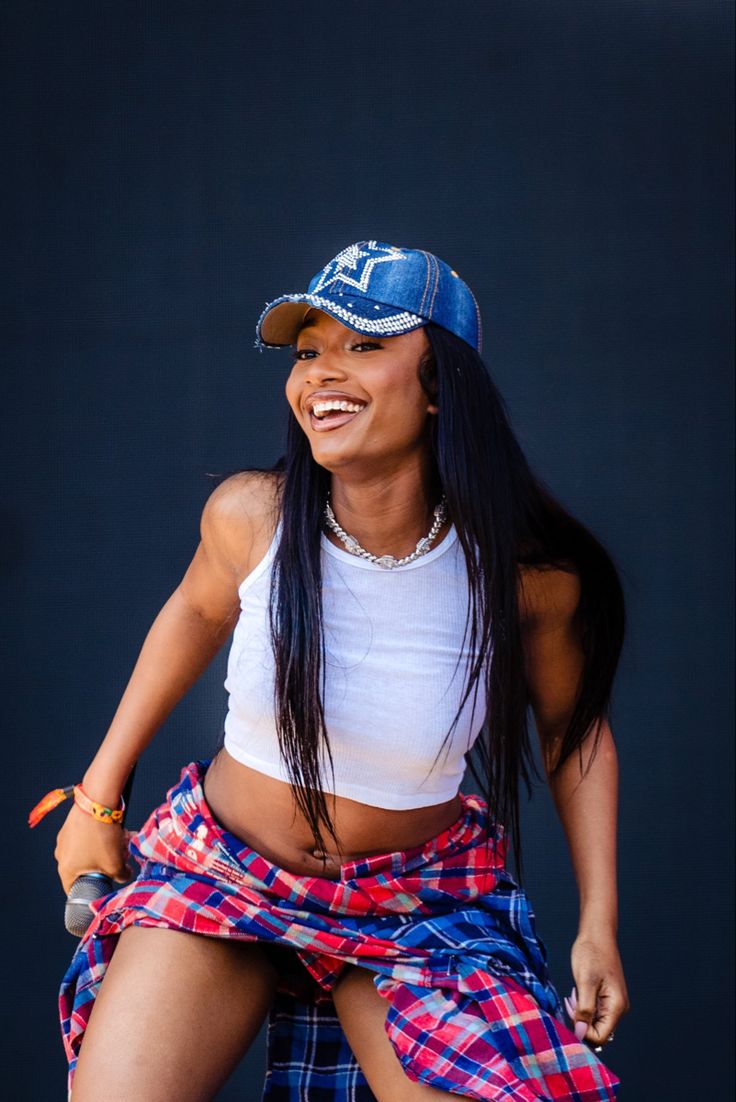 a woman wearing a plaid skirt and a blue cap smiles as she sits on a stage