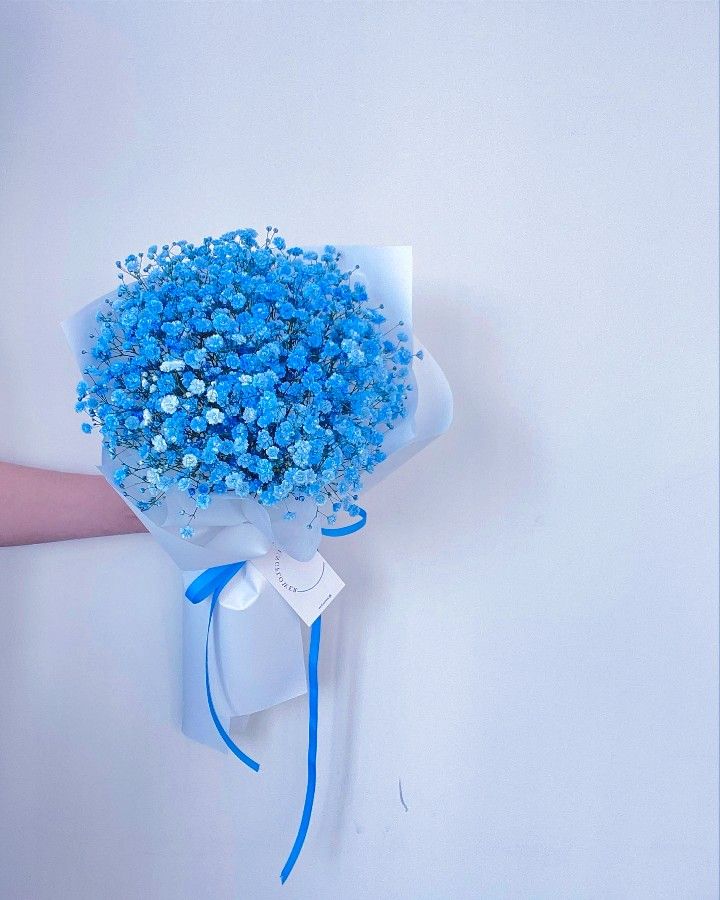 a bouquet of blue flowers is tied to the side of a wall with a person's hand holding it