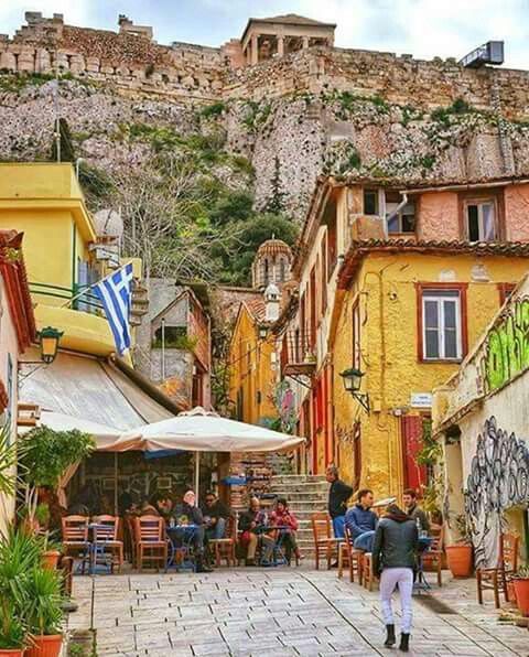 people are sitting at tables in an alleyway with buildings on the hill behind them