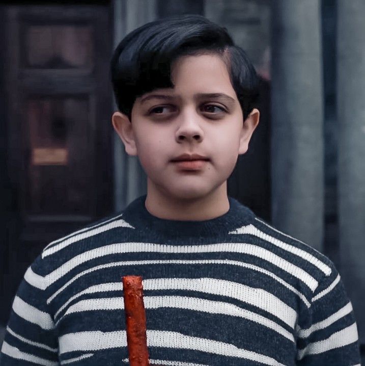 a young boy in a striped sweater holding an orange object with one hand and looking at the camera