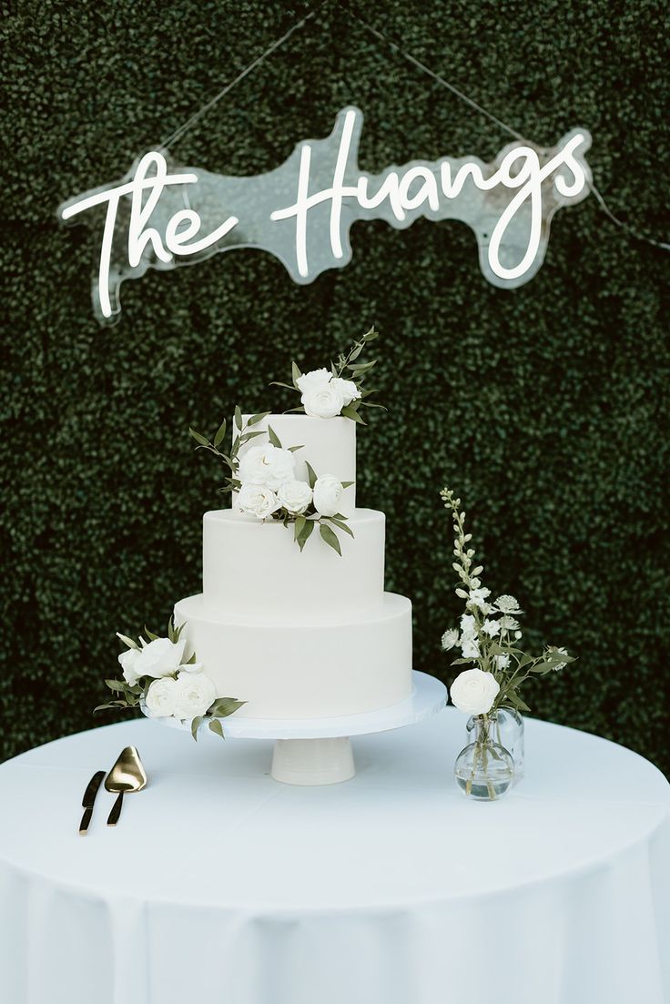 a white wedding cake sitting on top of a table next to a sign that says the hungs