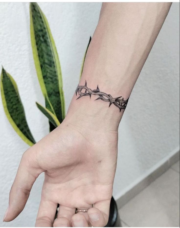 a woman's hand with a tattoo on it and a plant in the background