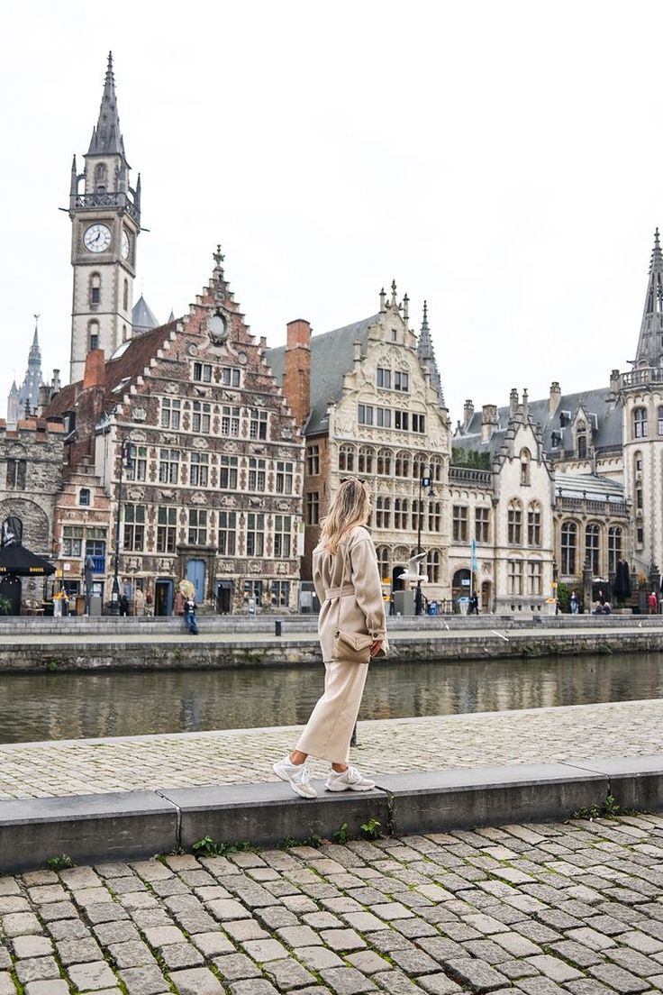 a woman standing on the edge of a brick walkway in front of buildings and a clock tower