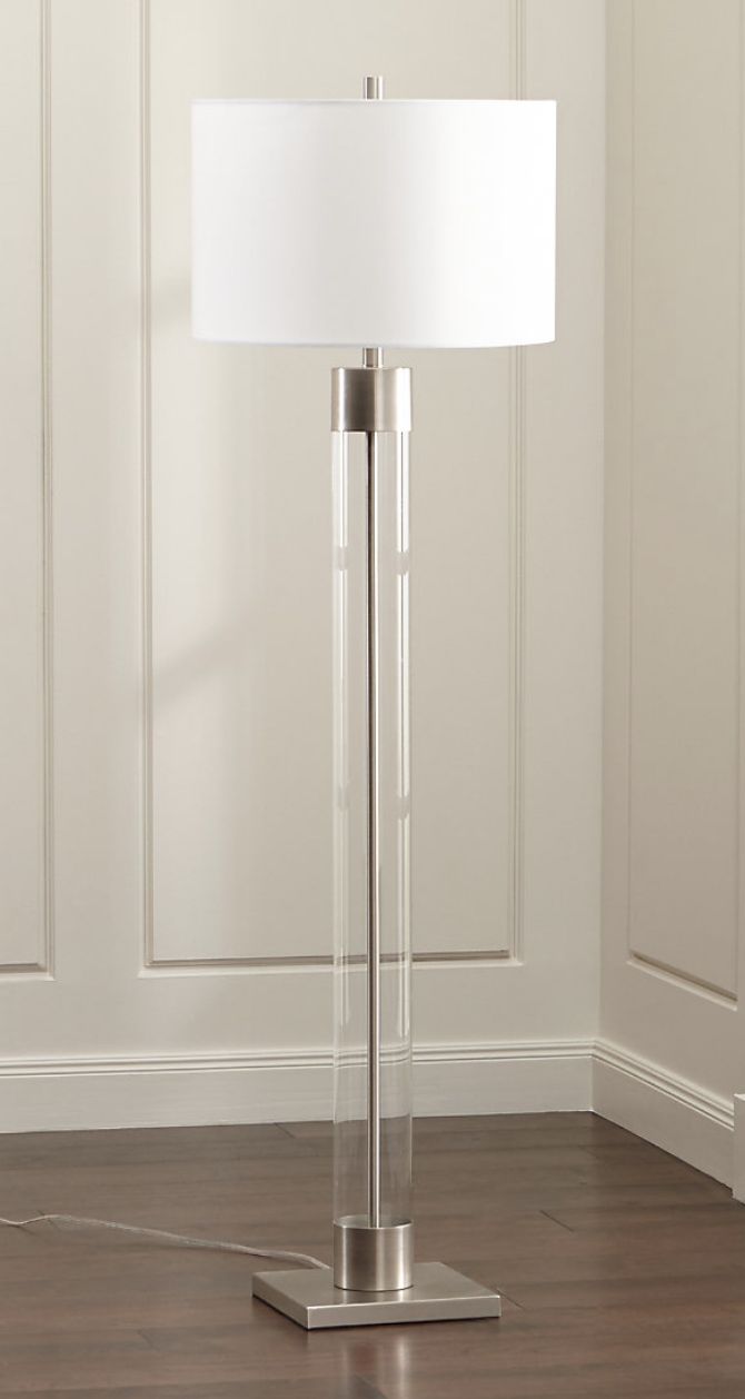 a floor lamp with a white shade on it in front of a wooden floor and wall