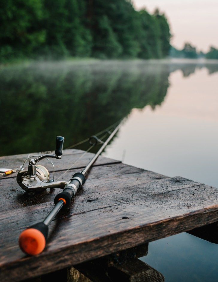 a fishing rod and reel on a wooden dock next to the water with trees in the background