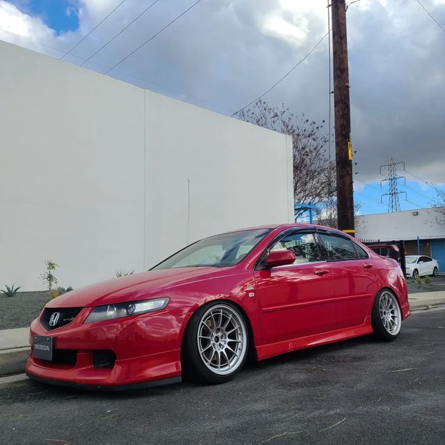 a red car parked on the street next to a white building and power lines in the background