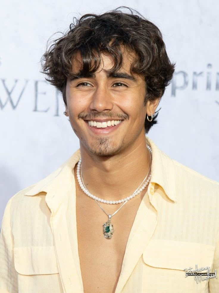 a man with a pearl necklace smiling at the camera while wearing a yellow shirt and pearls around his neck