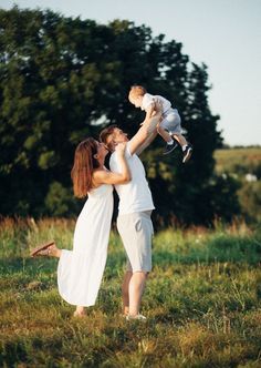 a woman holding a baby in her arms while standing next to a man on the grass