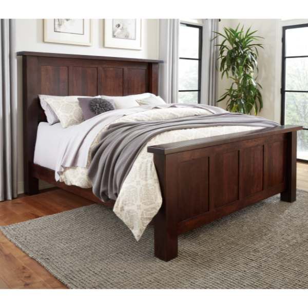 a bed with wooden headboard and foot board in front of two windows, rug on the floor