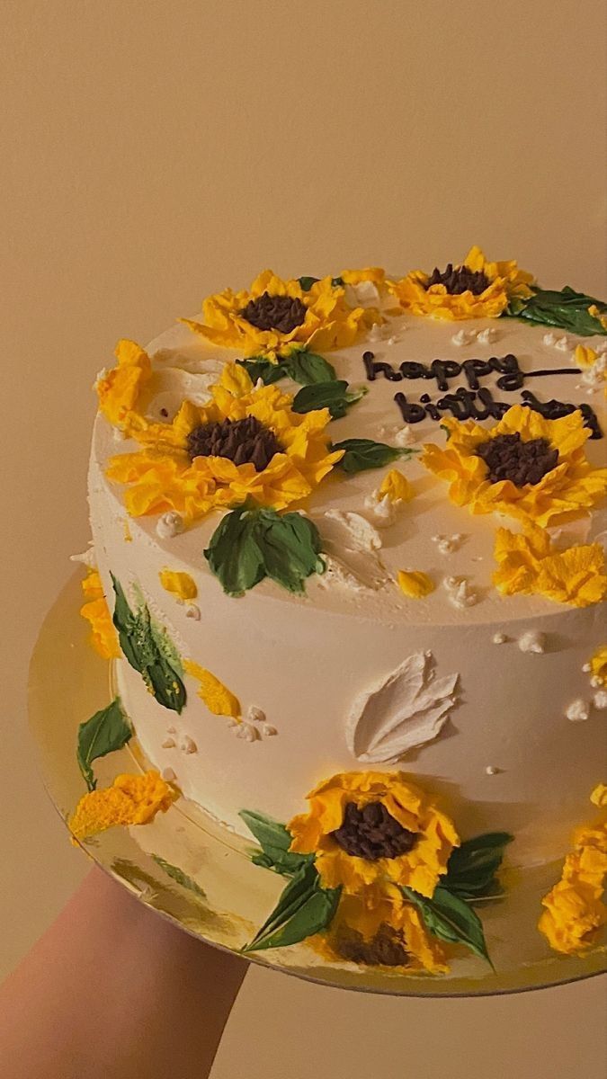 a cake with sunflowers on it being held by a person's hand