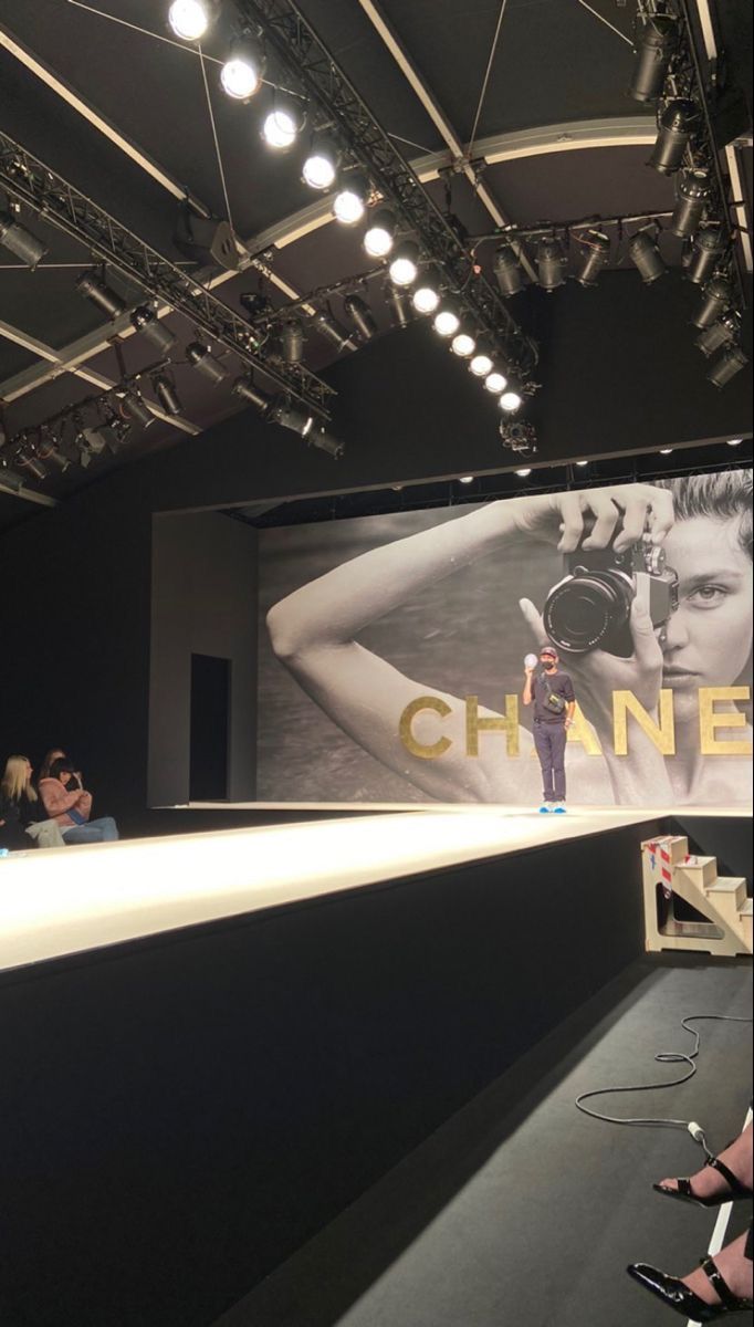 people are sitting in front of a chanel advertisement on the wall at a fashion show