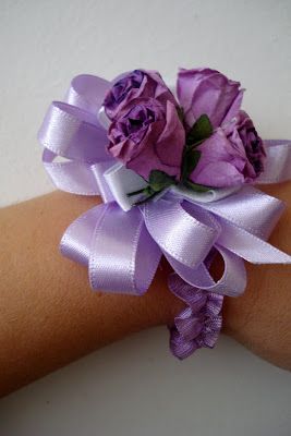 a woman's arm wearing a purple wrist corsage with flowers on it