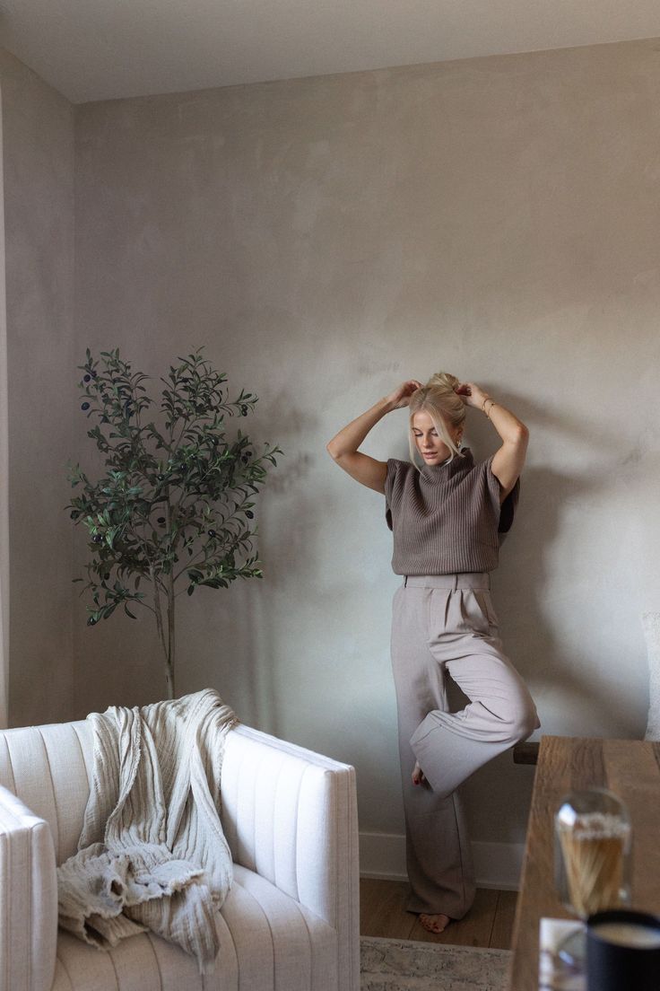 a woman standing in front of a white couch next to a potted plant on top of a wooden table