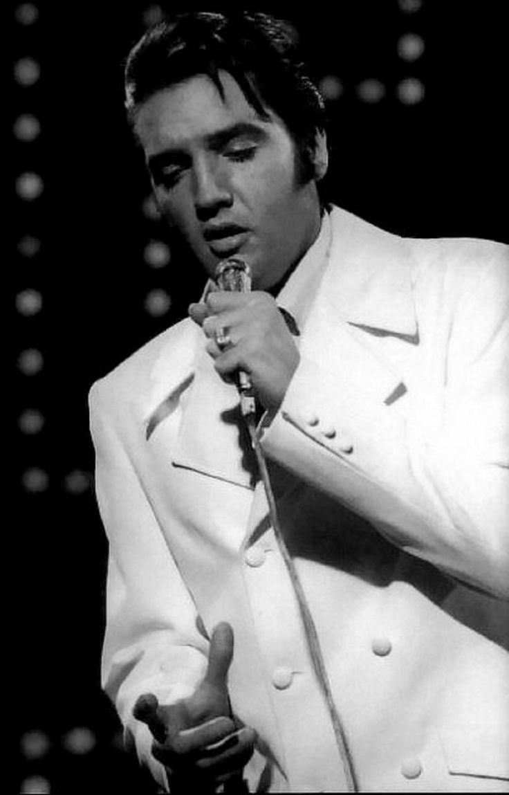 a man in a white suit holding a microphone and making a gesture with his hand