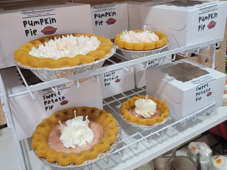 several pies on display in a bakery with white boxes behind them and one is topped with whipped cream