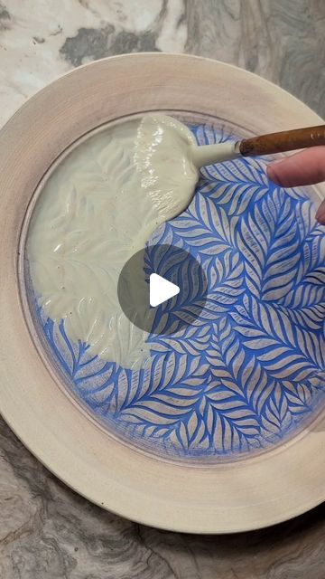 someone is painting a bowl with blue leaves on it