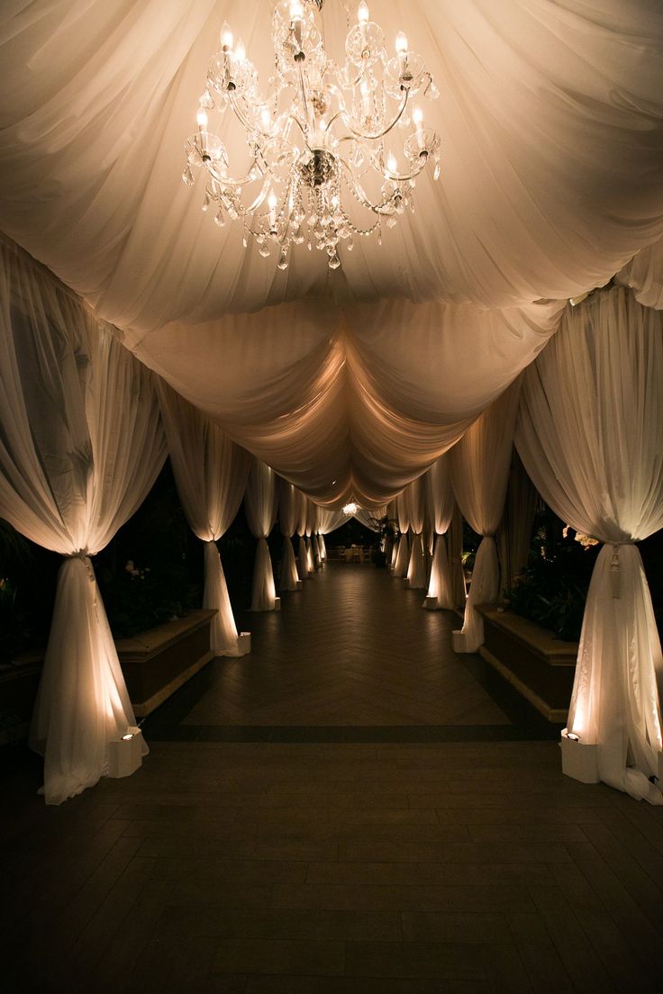 an image of a wedding venue with white drapes and chandeliers on the ceiling