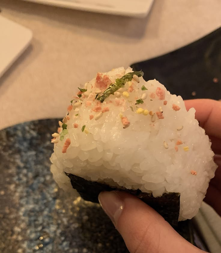 a person holding up a sushi with rice and garnishes on it