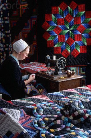 a woman sitting at a sewing machine in front of a quilt