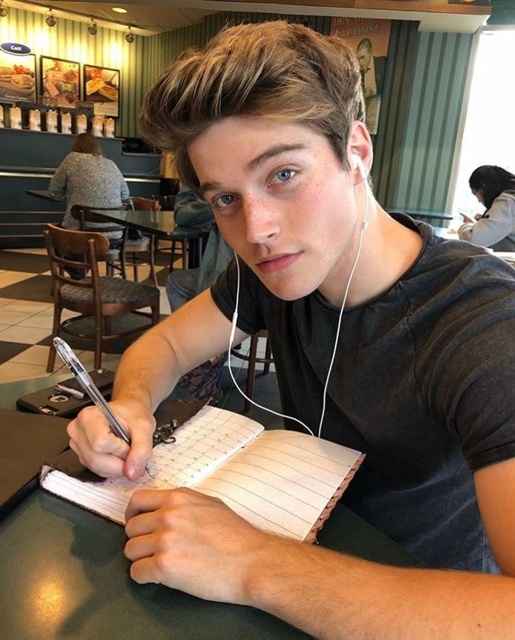 a young man sitting at a table with headphones on and writing in a notebook