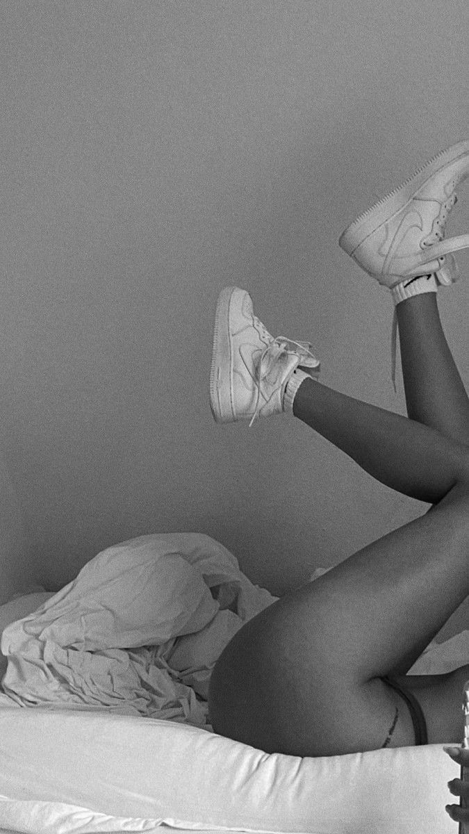 a black and white photo of a woman laying in bed with her feet up on the pillow