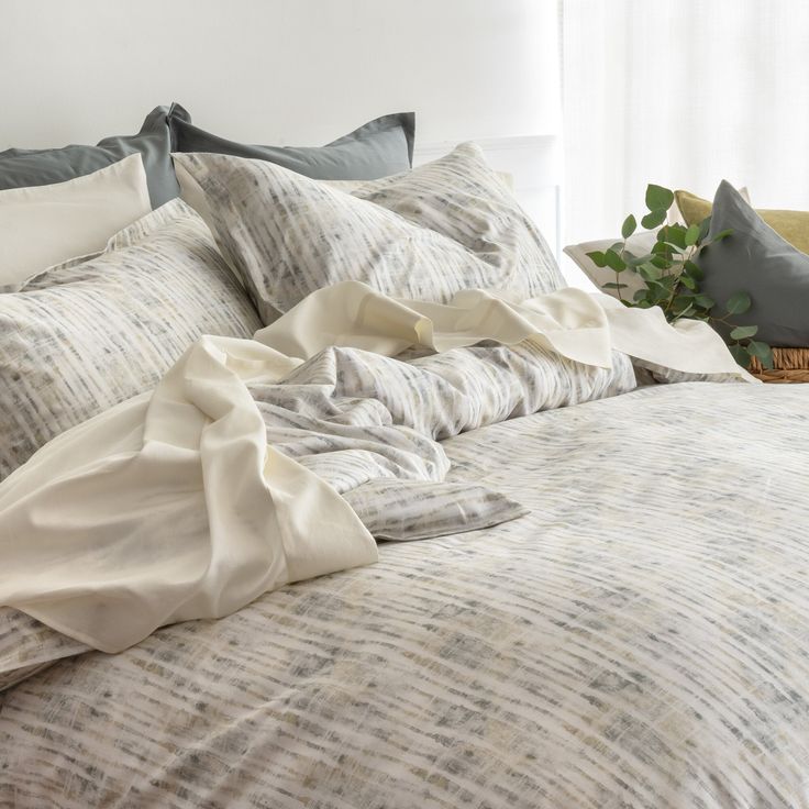 an unmade bed with grey and white sheets, pillows and blankets on top of it