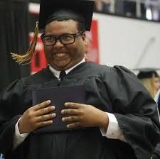 a graduate smiles as he holds his diploma