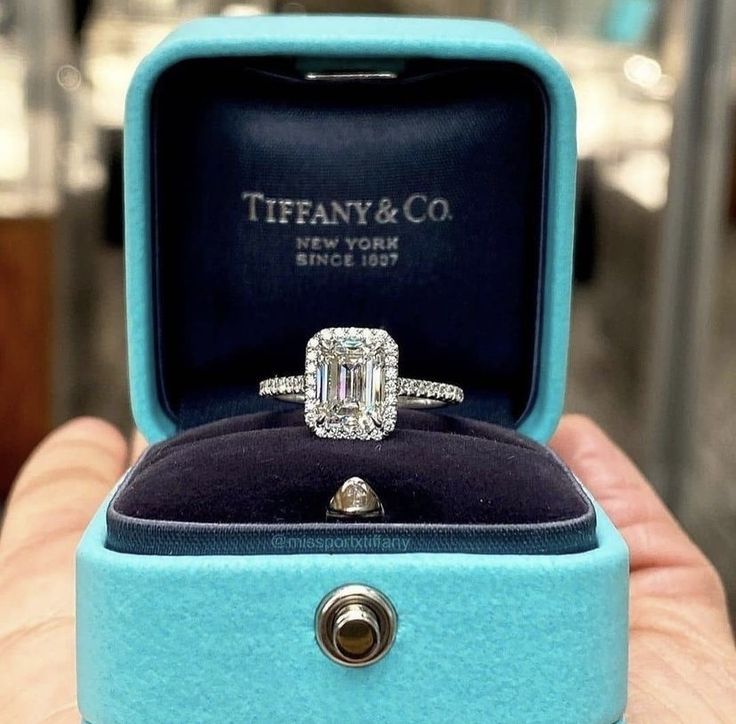 a person holding an engagement ring in a blue box with the words tiffany & co on it