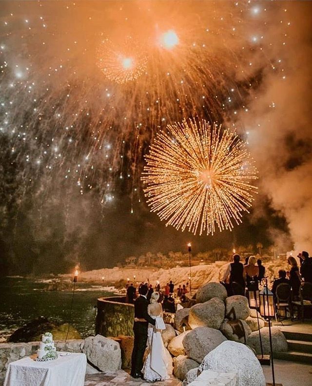 fireworks are lit up in the night sky above a wedding party on rocks and water